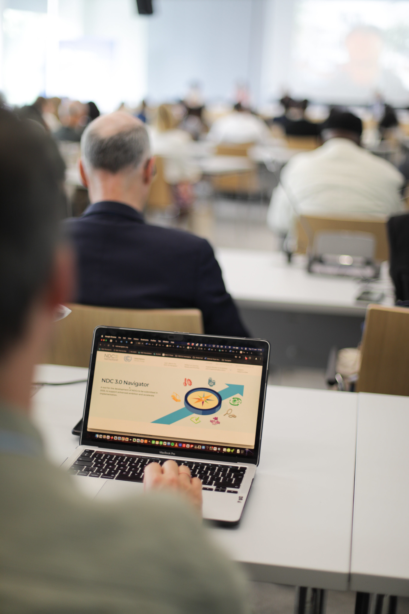 A person is seen using a laptop to explore the NDC 3.0 Navigator. The website's interface shows several categories related to climate action, including "Routes That Help Countries Reflect on the First Global Stocktake and Enhance NDC Ambition."